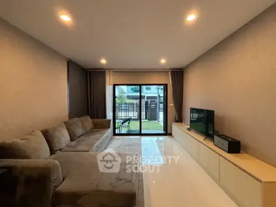 Modern living room with large sofa and entertainment center, featuring sliding glass doors to garden view.