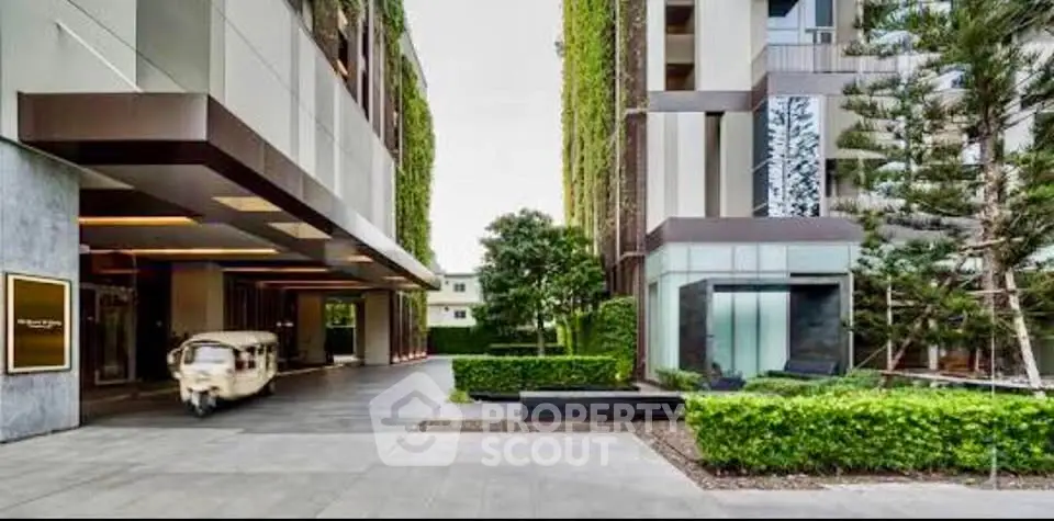 Modern building entrance with lush greenery and unique architectural design.