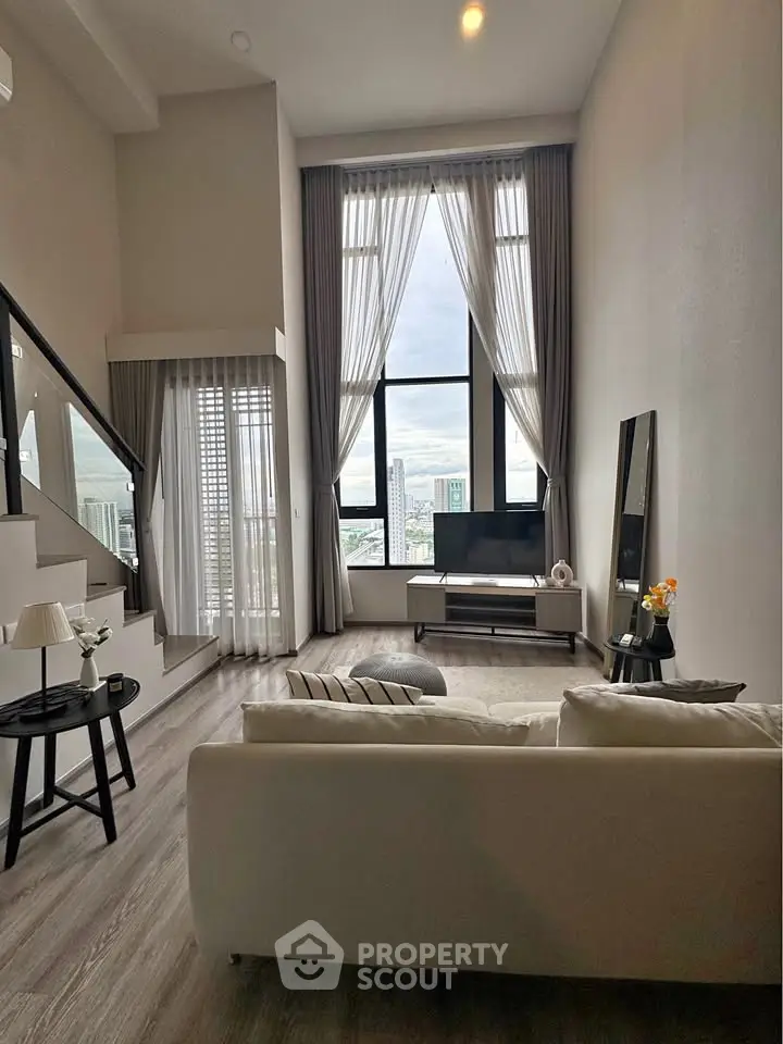 Spacious modern living room with high ceilings and large windows offering city views.