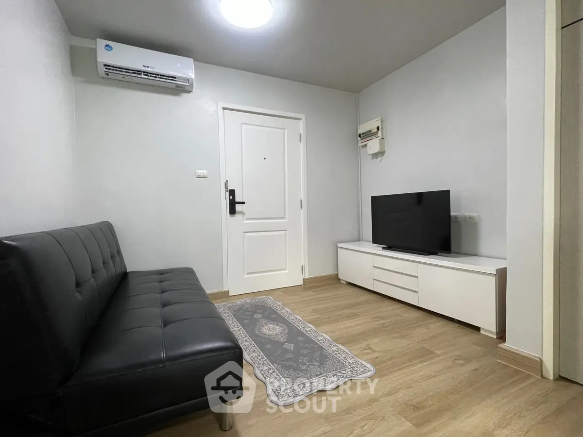 Modern living room with sleek black sofa and flat-screen TV on wooden flooring.