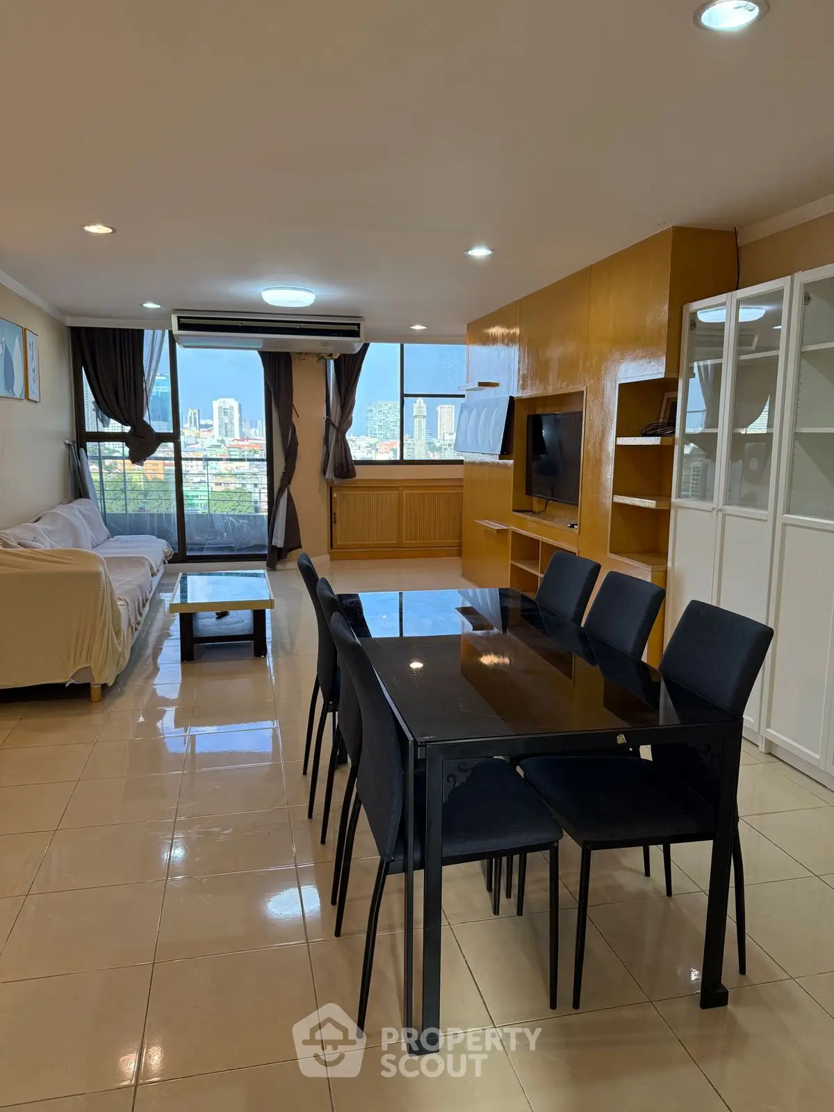 Spacious living room with dining area and city view, featuring modern furniture and large windows.