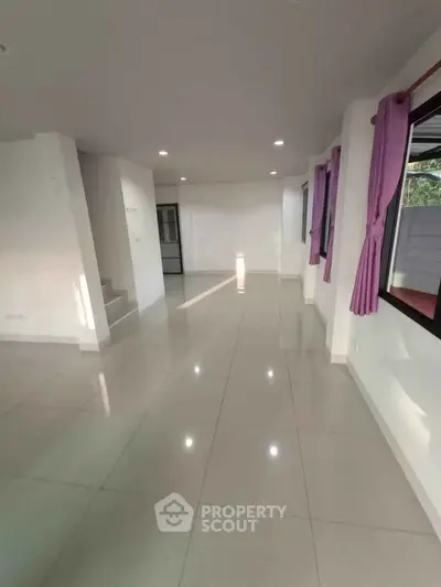 Spacious open-plan living area with glossy tiled floors and large windows.