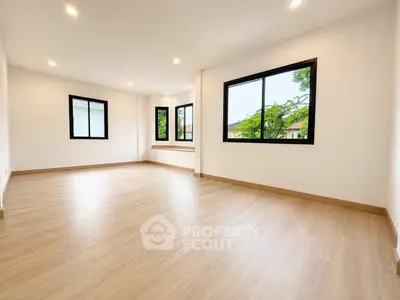 Spacious empty living room with large windows and wooden flooring, perfect for customization.
