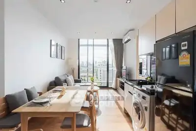 Modern open-plan living room with dining area and kitchen, featuring sleek appliances and a bright balcony view.