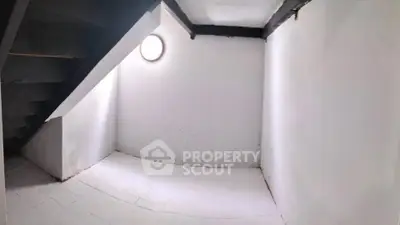 Spacious white-walled storage room with unique circular window under staircase.