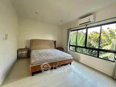 Spacious bedroom with large window and lush greenery view, featuring modern air conditioning.