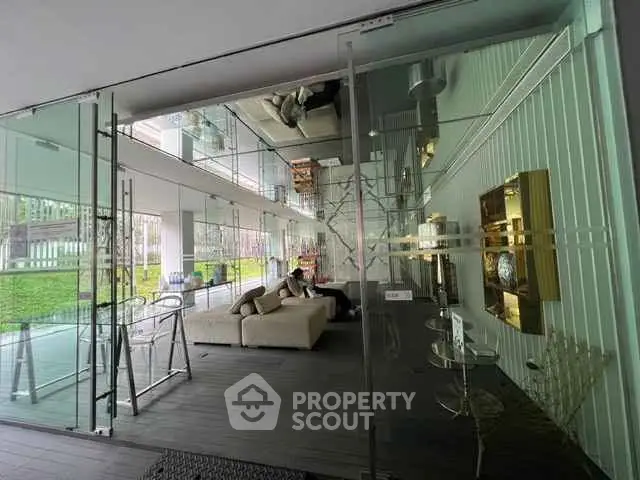 Modern glass-walled living area with stylish furniture and green outdoor view.