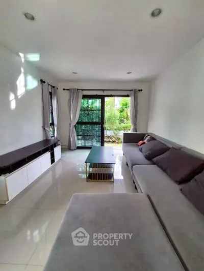Spacious living room with modern sofa and large windows overlooking a lush garden.