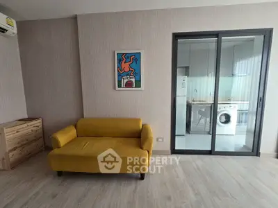 Modern living room with yellow sofa and view into kitchen with washing machine.