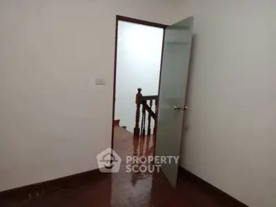Minimalist interior room with open door leading to staircase, showcasing polished wooden flooring.