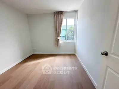 Spacious empty room with wooden flooring and natural light from window