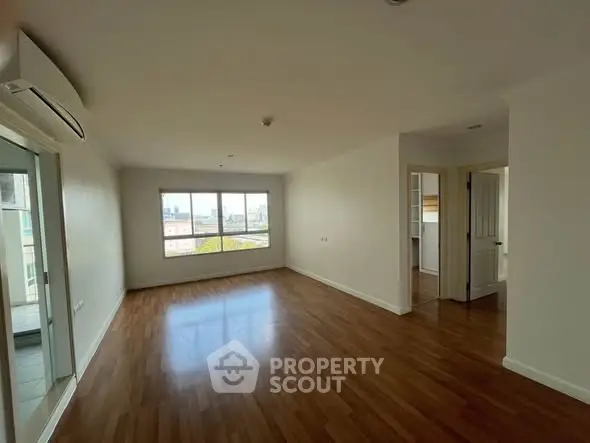 Spacious empty living room with wooden flooring and large window view.