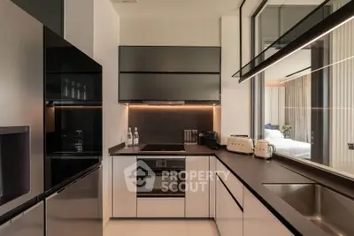 Modern kitchen with sleek black and white cabinetry, built-in appliances, and a view into the bedroom.