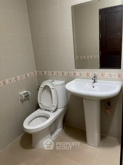 Modern bathroom with pedestal sink and toilet, featuring neutral tile design.